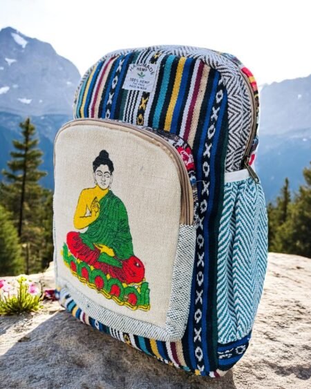 Handmade hemp and cotton backpack with Buddha art print, featuring tribal Himachali fabric details, placed in front of a natural mountain landscape from Kasol, Himachal