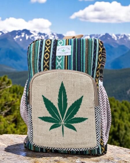 Handcrafted backpack made from cotton and hemp fabric with green hemp leaf print, featuring Himachali tribal design, placed on a rustic wooden table in the Himalayan outdoors