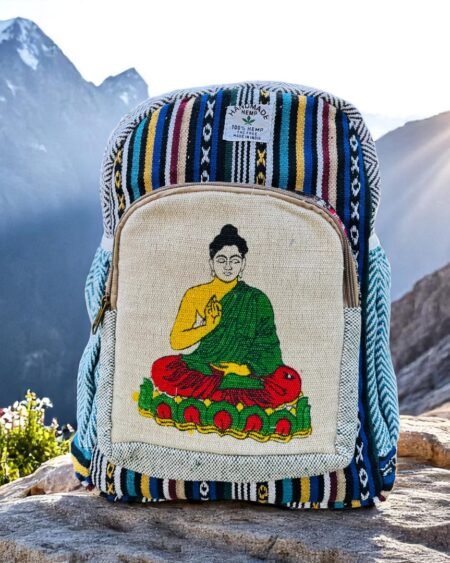 Handmade hemp and cotton backpack with Buddha art print, featuring tribal Himachali fabric details, placed in front of a natural mountain landscape from Kasol, Himachal