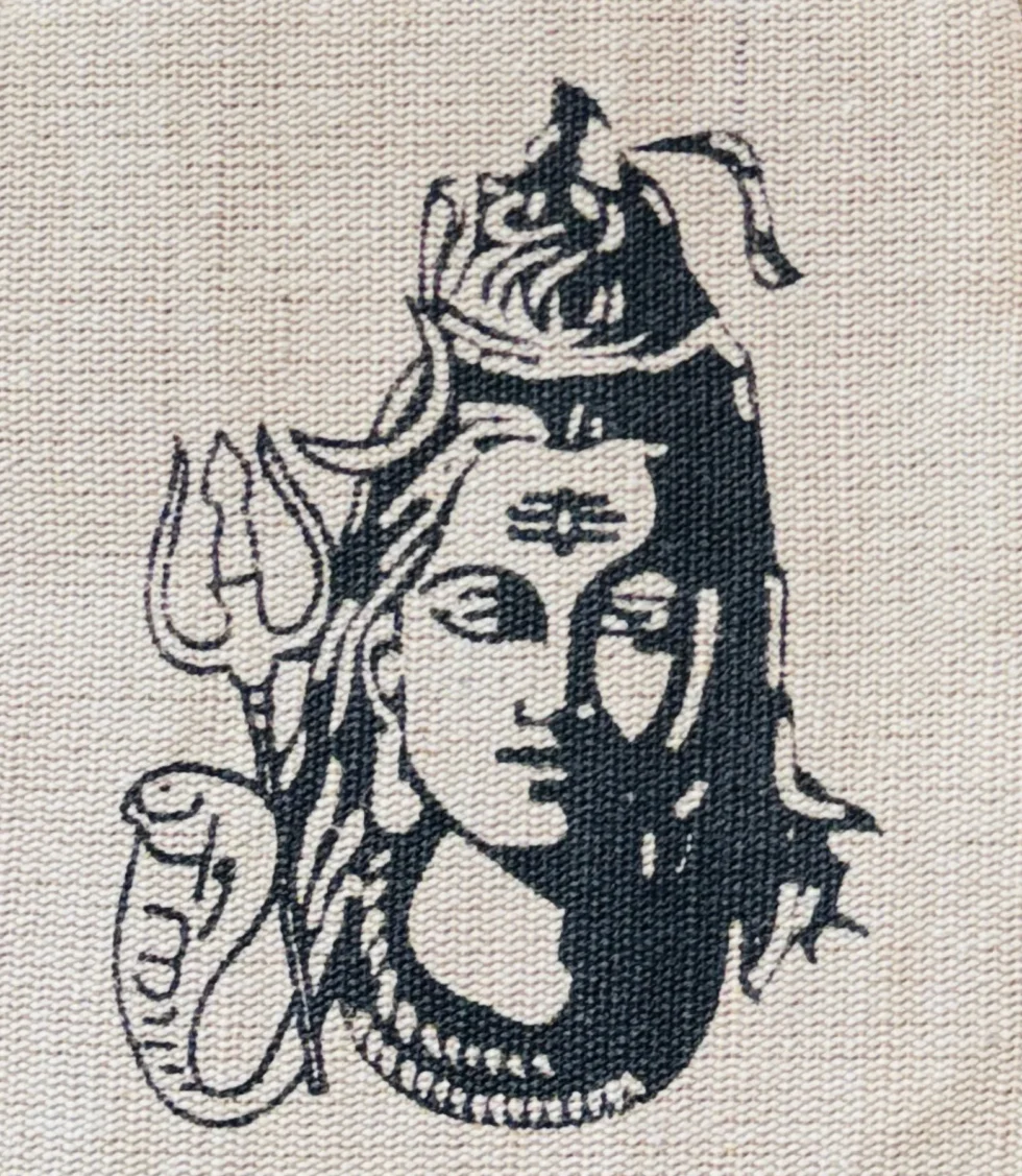 Handmade cotton and hemp backpack with Lord Shiva print, featuring colorful Himachali tribal patterns, placed on a rock with a scenic Himalayan lake and mountains in the background