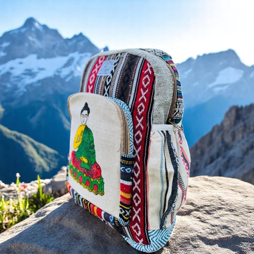 Handmade hemp and cotton backpack with Buddha art print, featuring tribal Himachali fabric details, placed in front of a natural mountain landscape from Kasol, Himachal